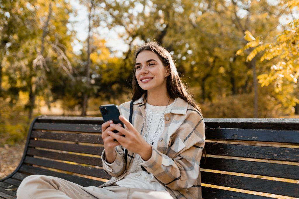 attractive young woman walking in autumn wearing jacket using phone